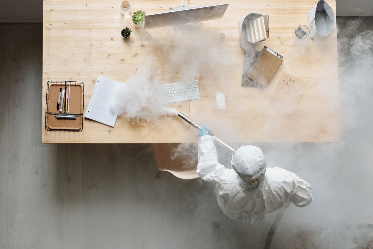 A person sanitizes a work area with fumigation while wearing full protective equipment for protection.